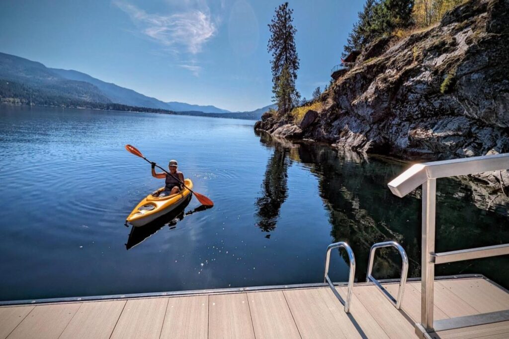 Home Guest paddling a yellow kayak on the calm blue waters of Christina Lake.
